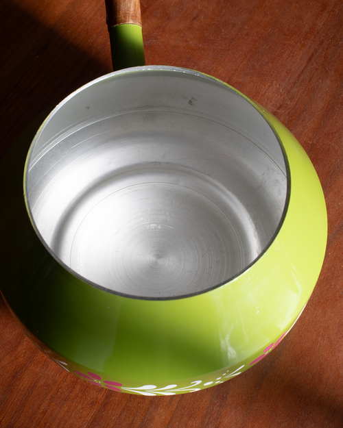 A close-up top-down view of a lime green saucepan with a brushed silver interior and a wooden handle, resting on a brown wooden surface.