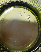 Close-up of the bottom of a vintage green glass bottle or jar, showing embossed text reading 'F.T.