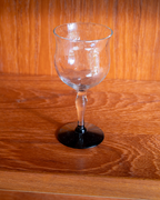 A clear glass goblet with a black circular base, standing on a polished wooden surface against a wooden background.