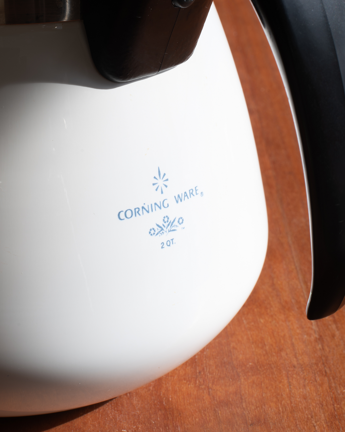 Close-up of a white Corning Ware 2 oz ceramic mug with blue printed branding, resting on a wooden surface.