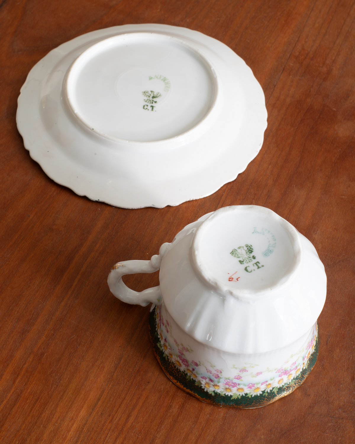 A white porcelain teacup with a floral pattern around the base, shown upside down next to its matching white saucer on a wooden table.