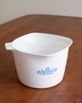 A white ceramic mixing bowl with a blue floral pattern, sitting on a wooden table.
