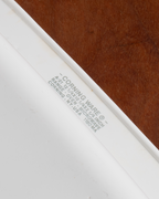 Close-up of a white ceramic or stoneware microwave oven door trim with printed gray text reading 'CORNING WARE' and model information, set against a brown wood-grain surface.