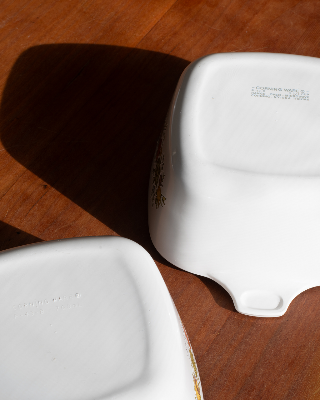 Two white ceramic baking dishes shown upside down on a wooden surface, displaying their non-stick coated interiors and printed safety markings.