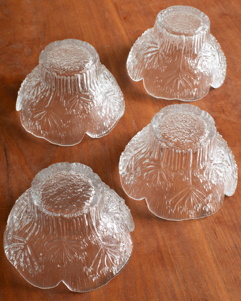 Four clear textured glass bowls arranged on a warm brown wooden surface.