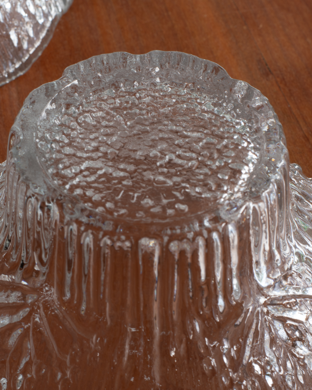 A close-up of a clear textured glass bowl or dish with a scalloped rim, photographed on a brown wooden surface.