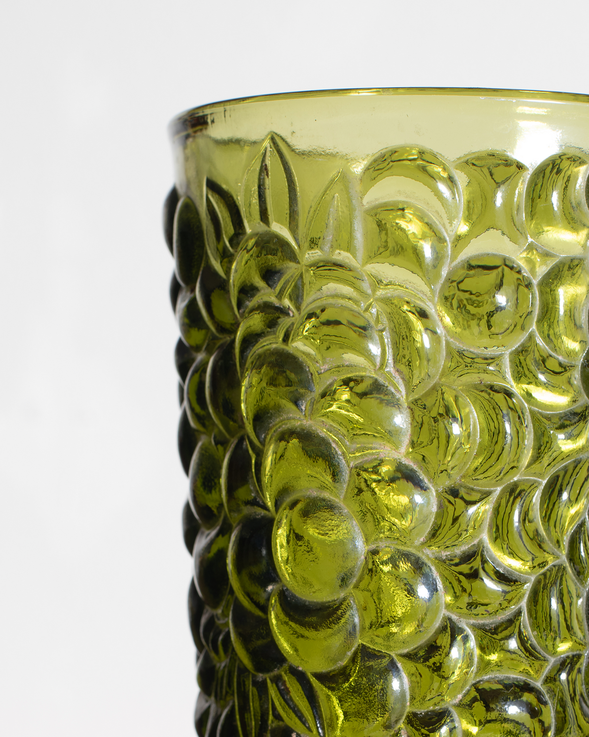 Close-up of a translucent olive green glass container with a textured, bubble-like embossed pattern on a white background.