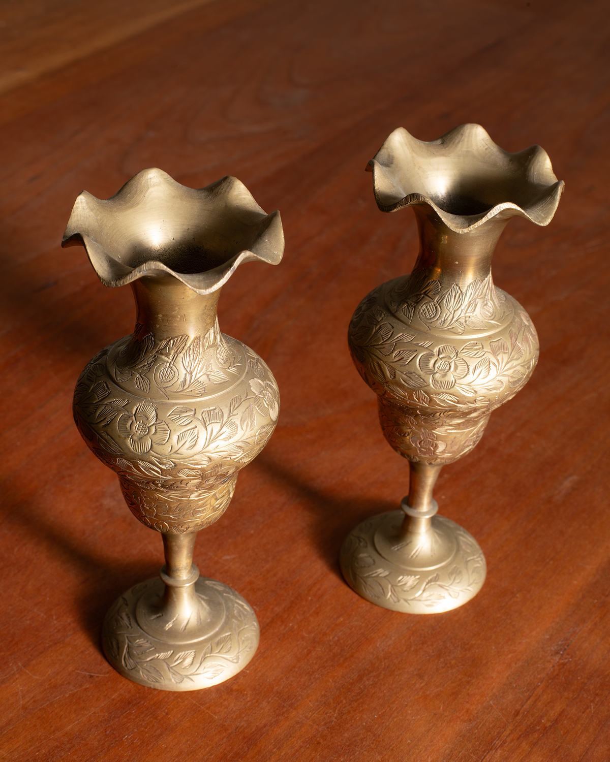 Two ornate brass flower-shaped goblets with floral engravings, displayed on a polished wooden surface.