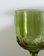 Close-up of an olive green glass goblet with a textured bubble pattern on the bowl, set against a neutral light gray background.