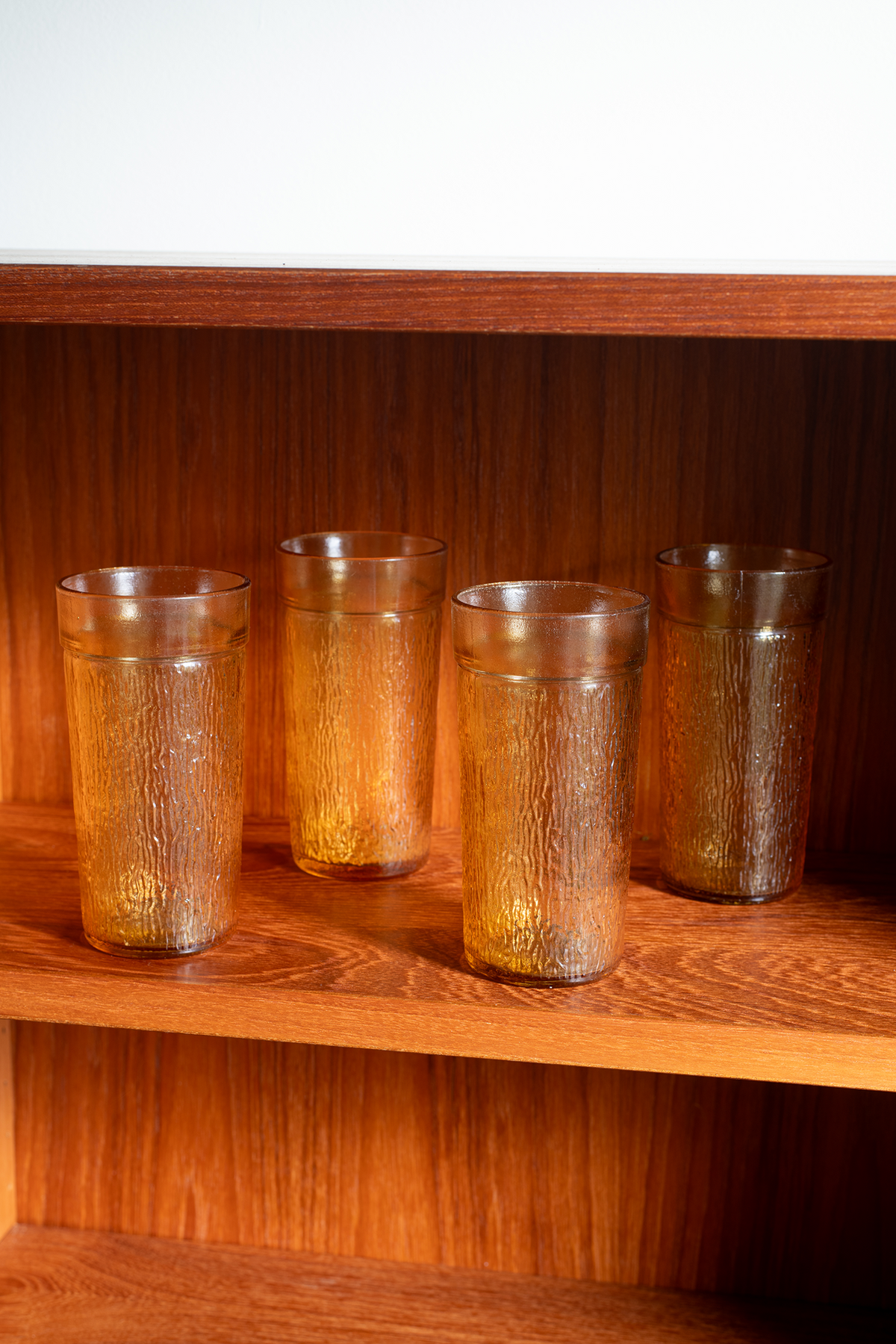 Four textured amber-brown glass tumblers displayed on a wooden shelf.