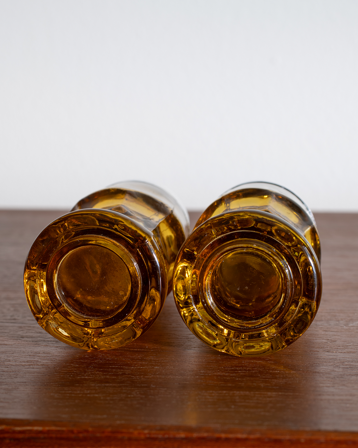 Two amber glass bottle bottoms or decorative glass pieces lying side by side on a dark wooden surface against a plain light background.