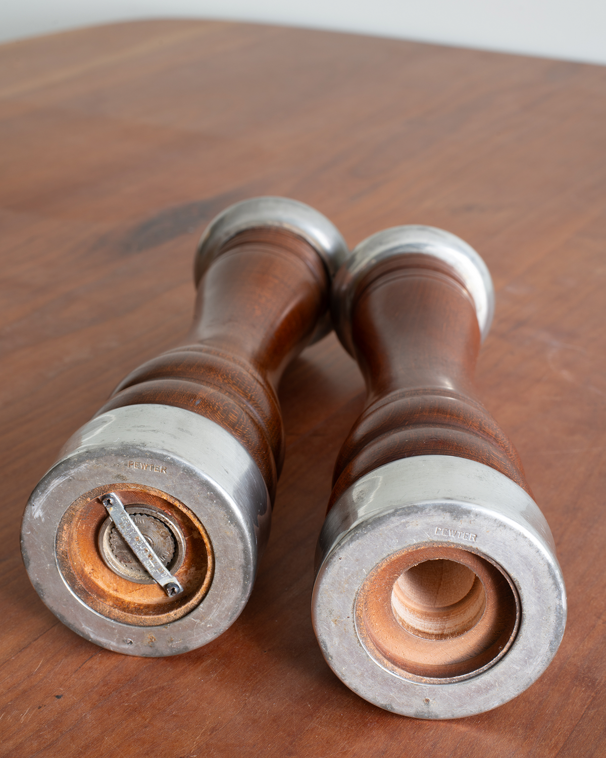 Two vintage wooden pepper mills with silver metal caps resting on a wooden tabletop.