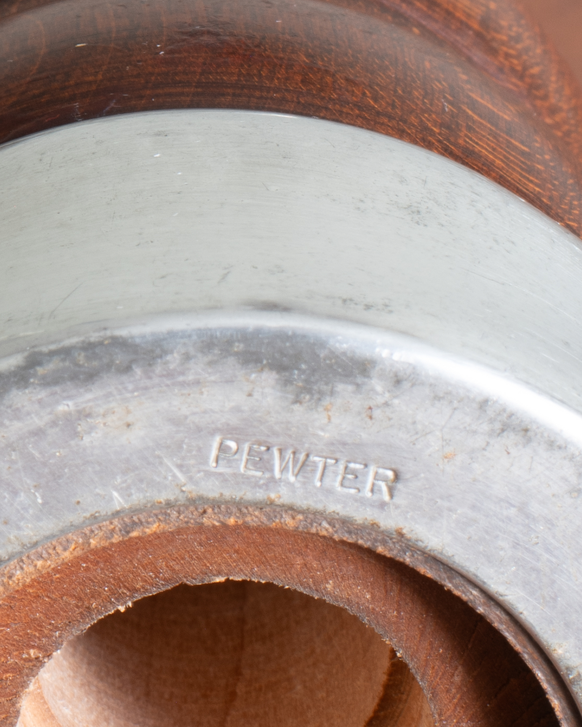 Close-up of a metal pipe fitting with the word 'PEWTER' embossed on the silver band, surrounded by a rusted brown interior.