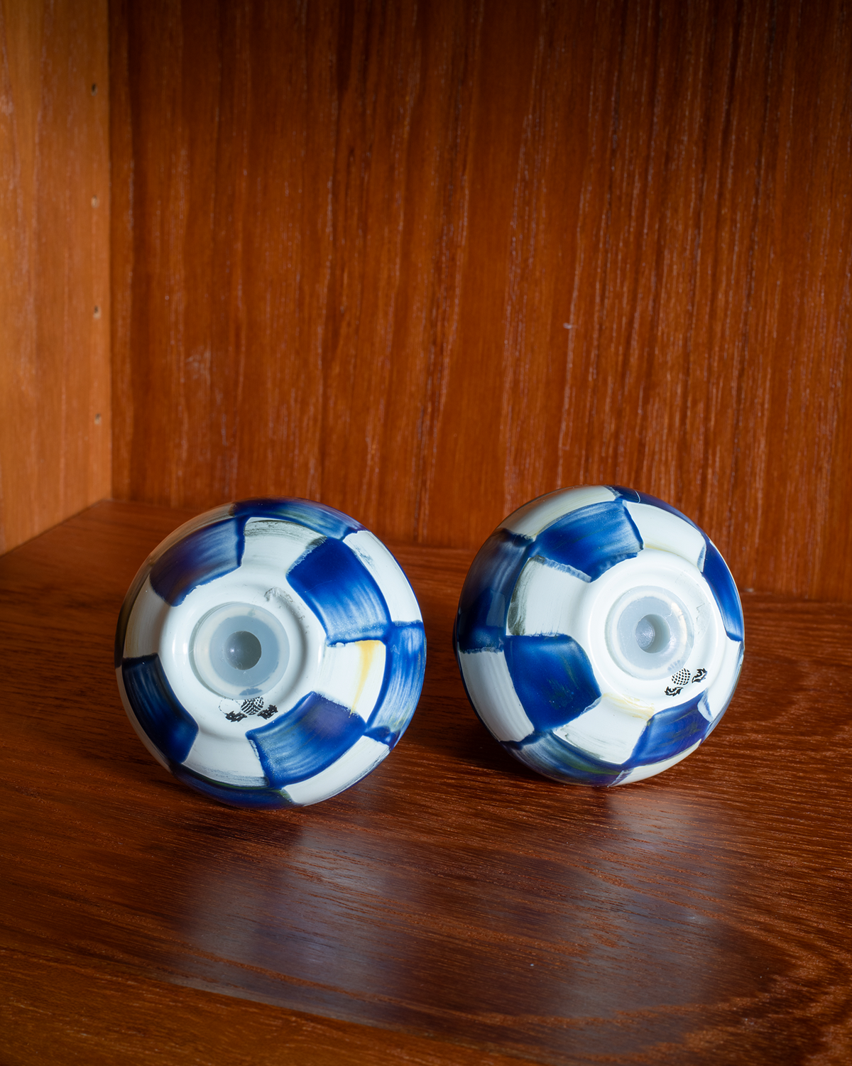 Two small round ceramic objects with a blue and white patchwork pattern, photographed on a wooden surface against a wooden background.