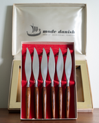 Six Mode Danish wooden-handled knives displayed in an open presentation box with a red velvet interior, with the branded outer box open behind it on a tabletop.