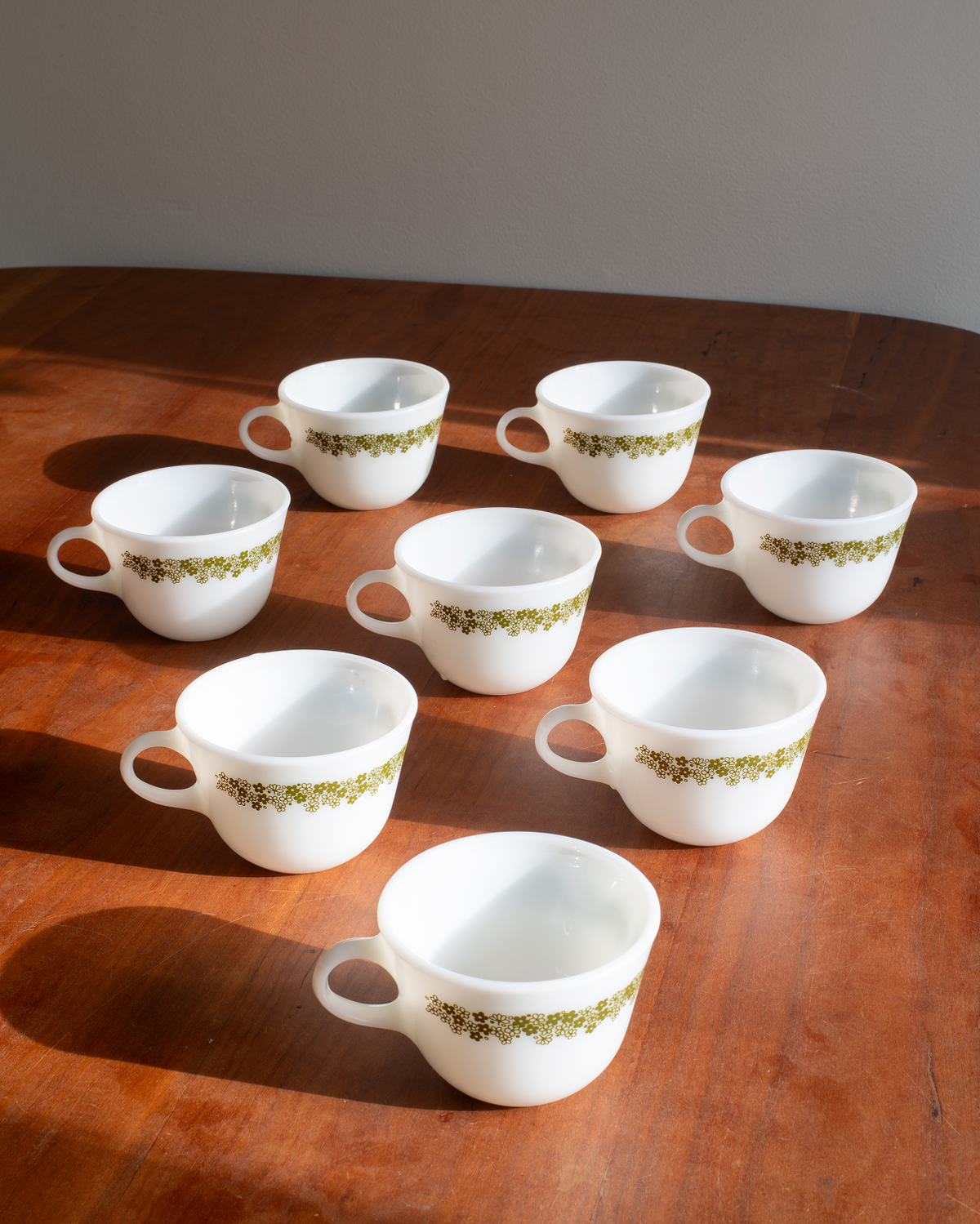 Six white ceramic coffee cups with a green floral pattern band, arranged on a wooden table.