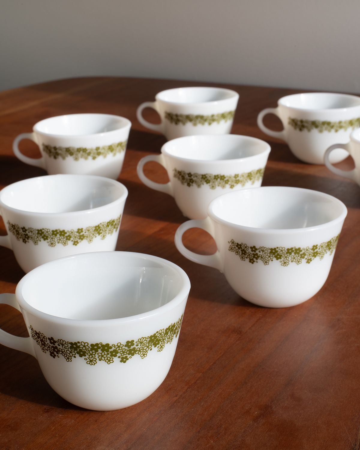 Six white ceramic teacups with a green floral pattern band, arranged on a dark wooden table.