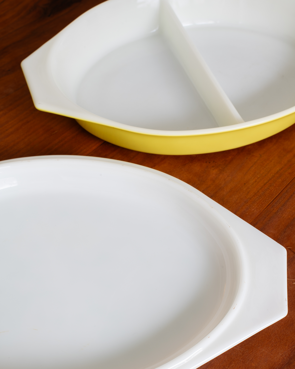 A white ceramic divided serving dish with a yellow rim, shown on a wooden surface with its matching white lid in the foreground.