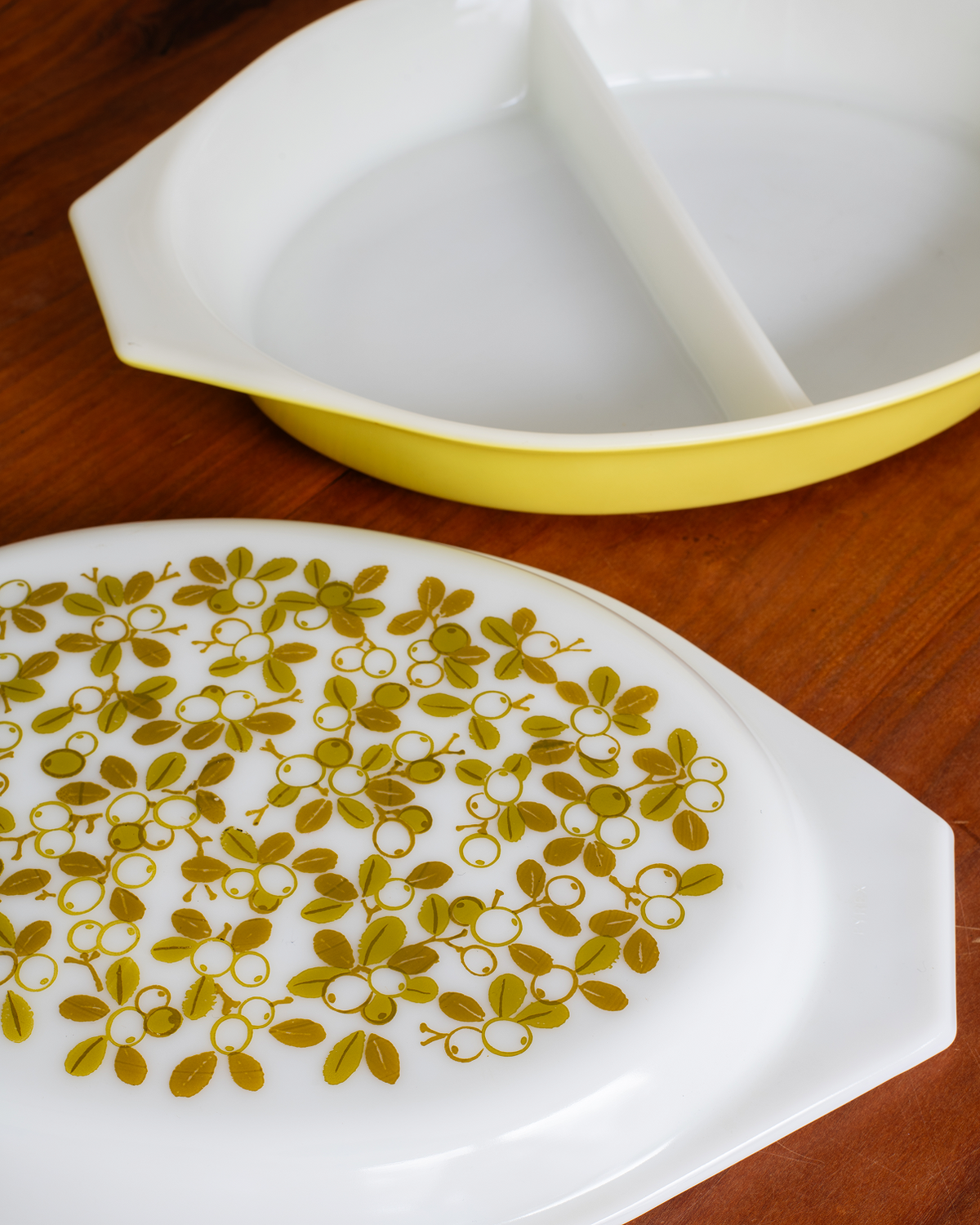 A white ceramic divided serving dish with a yellow rim, shown alongside a matching white plate with a yellow floral pattern, set on a wooden table.