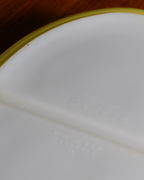Close-up of a white Pyrex glass container showing the embossed brand name and 'Shatter Proof' text, with a gold rim visible along the top edge.
