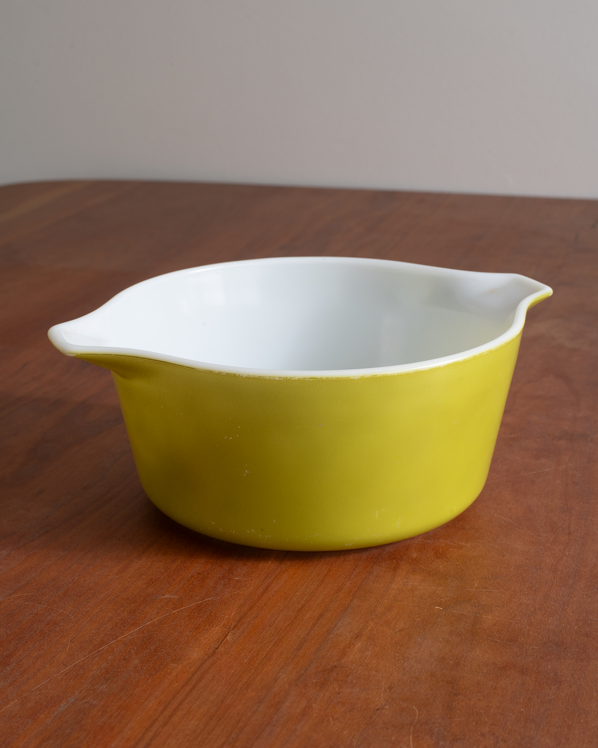 A yellow and white ceramic mixing bowl with a small pouring spout, resting on a wooden tabletop against a neutral background.
