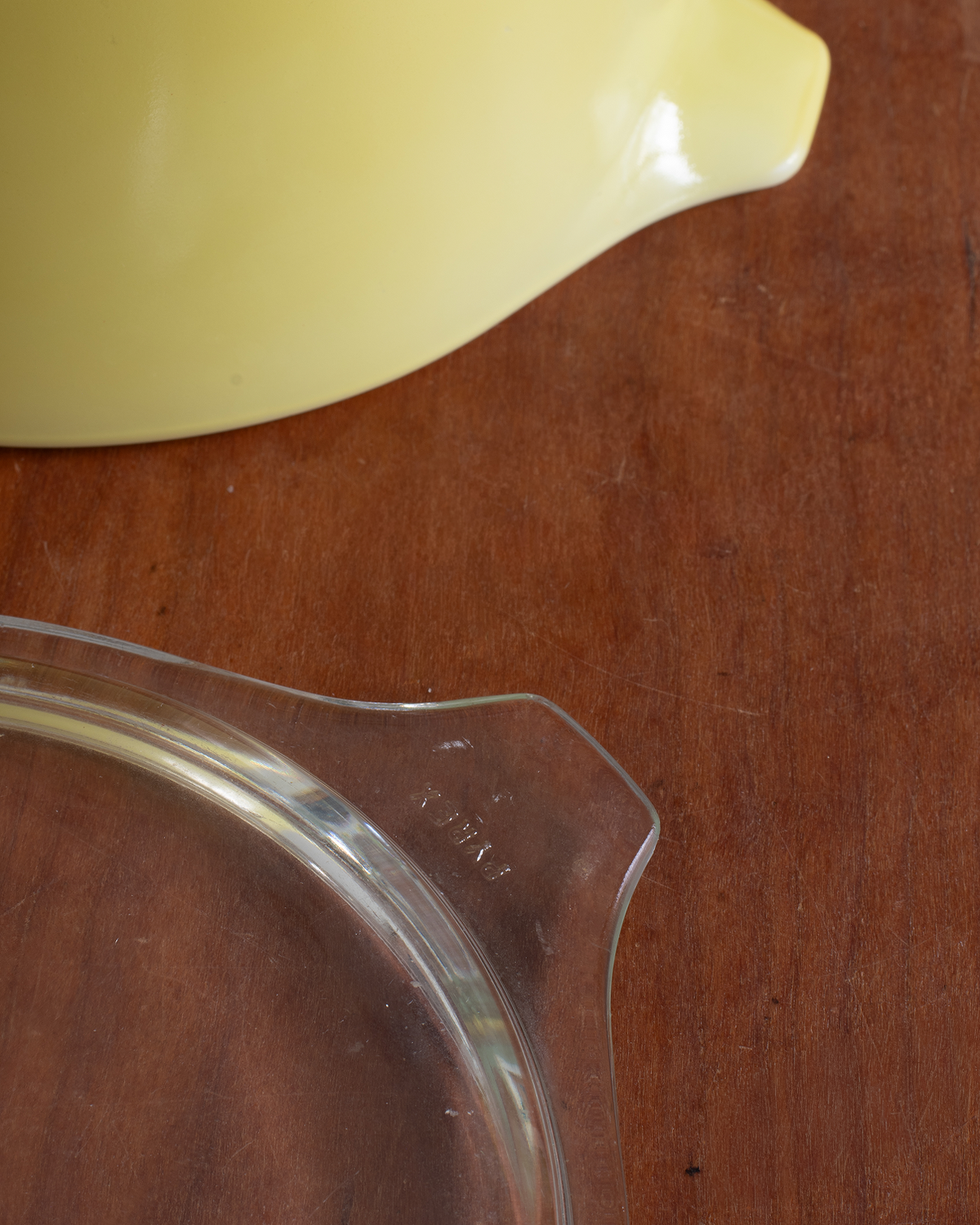 A close-up of a yellow ceramic bowl and a clear glass measuring cup on a brown wooden tabletop.