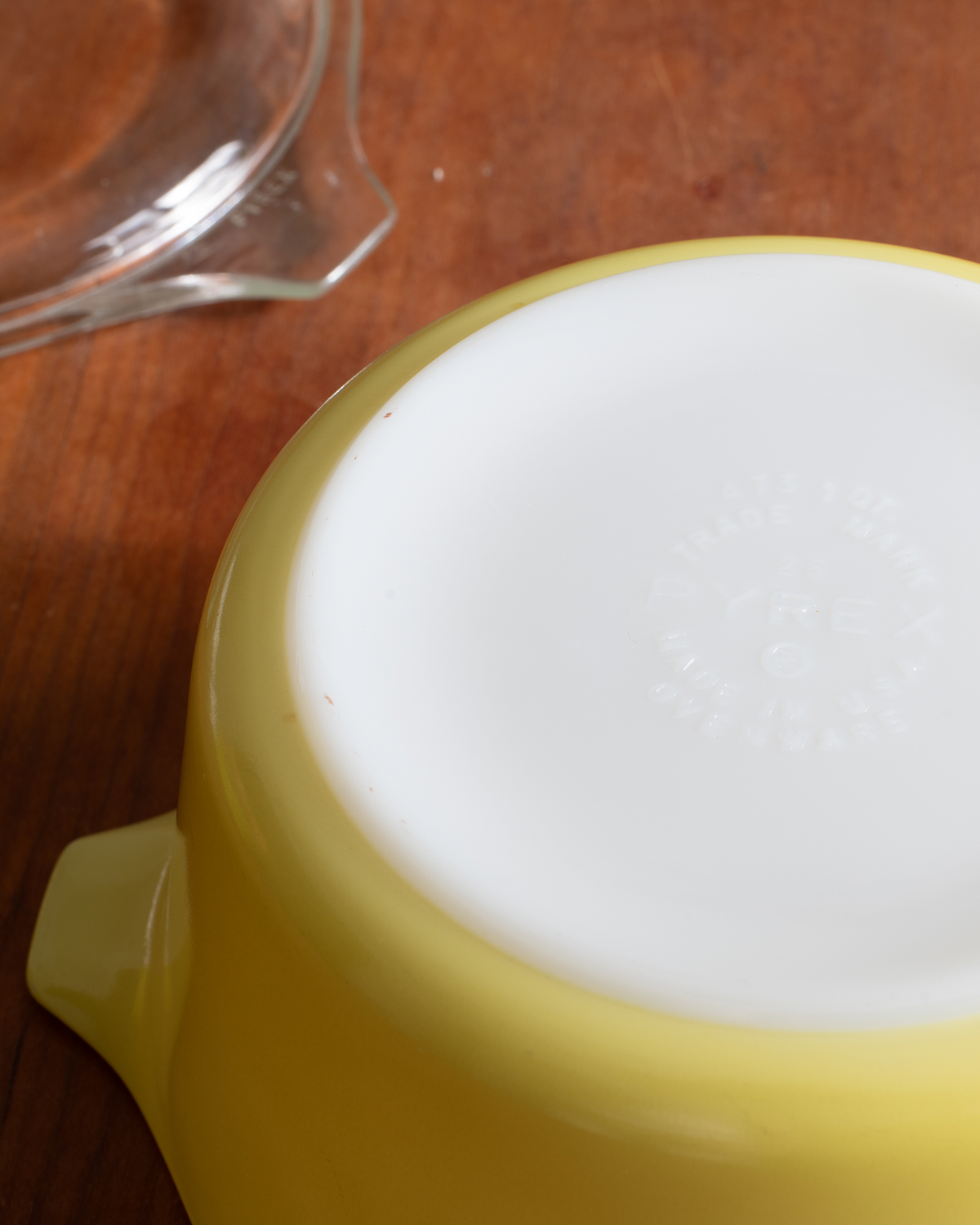 A close-up of a yellow glass bowl turned upside down on a wooden surface, showing a white glazed bottom with embossed branding.