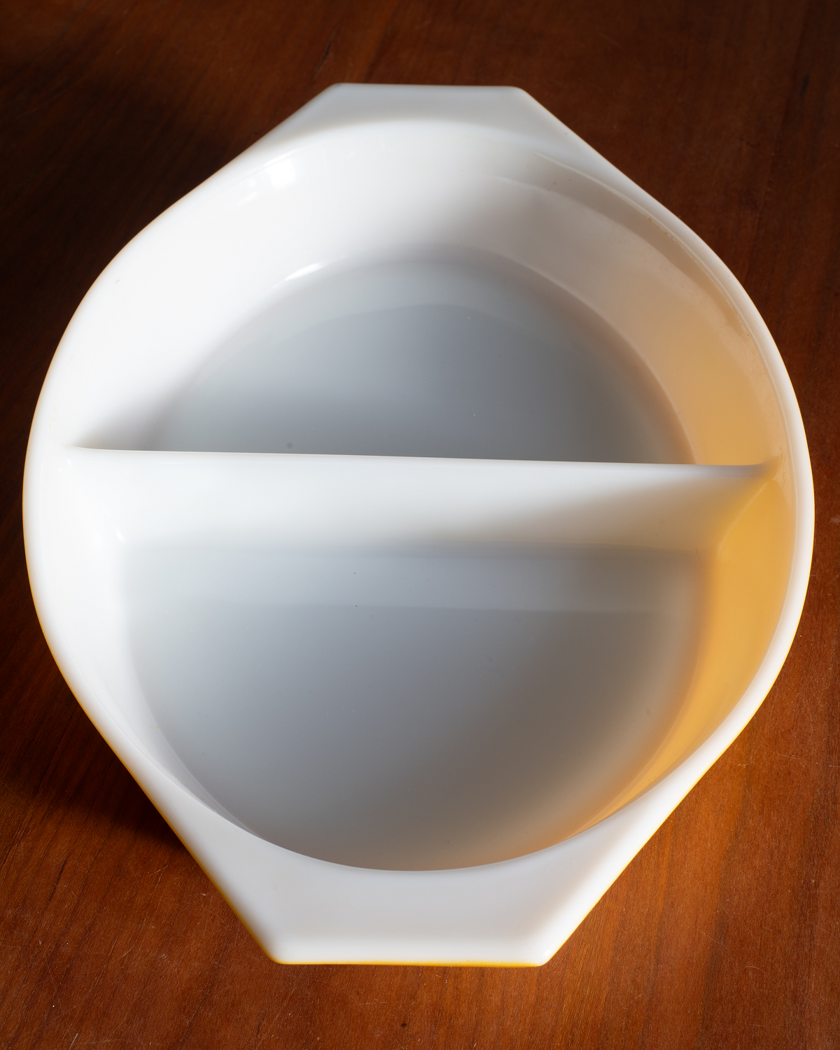 A white ceramic octagonal divided serving dish with a single horizontal隔板, shown on a dark brown wooden surface.