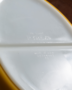 Close-up of a white Pyrex glass container lid with embossed brand text and a yellow rim, photographed against a dark brown background.
