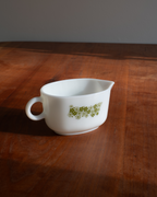 A white ceramic gravy boat with a small green floral pattern on the side, resting on a dark wooden table.