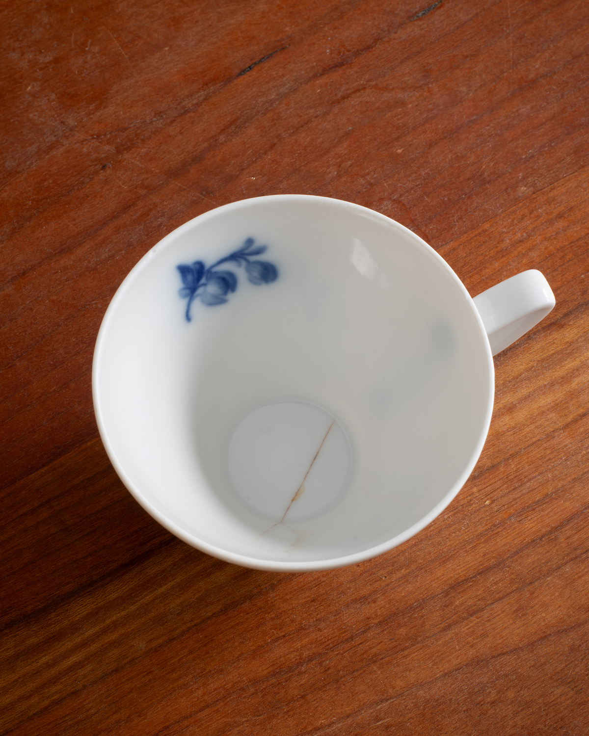 A white porcelain teacup with a blue floral pattern inside, shown from a top-down perspective on a wooden table.