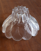 A vintage clear textured glass candle holder or lamp shade with a scalloped petal-like edge and ribbed center, shown on a wooden surface.