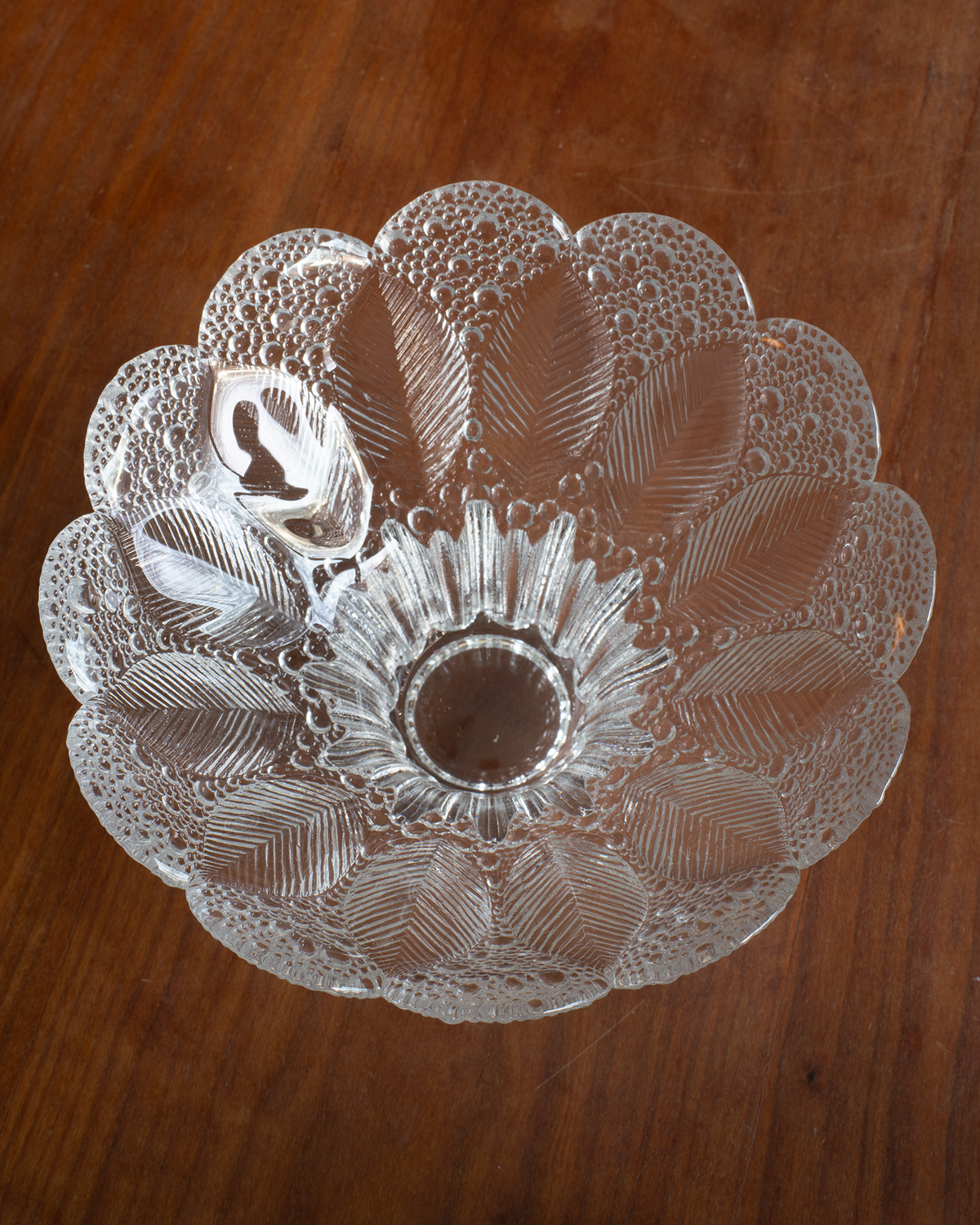 A clear glass bowl with a scalloped edge and embossed floral pattern, photographed from above on a brown wooden surface.