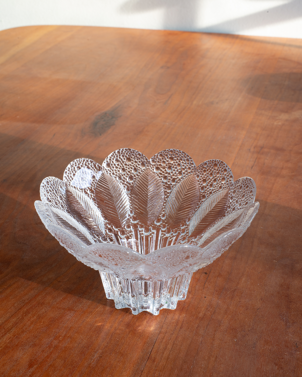 A clear cut-glass bowl with a scalloped rim and leaf-like pattern, placed on a wooden tabletop.