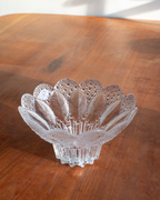 A clear cut-glass bowl with a scalloped rim and leaf-like pattern, placed on a wooden tabletop.