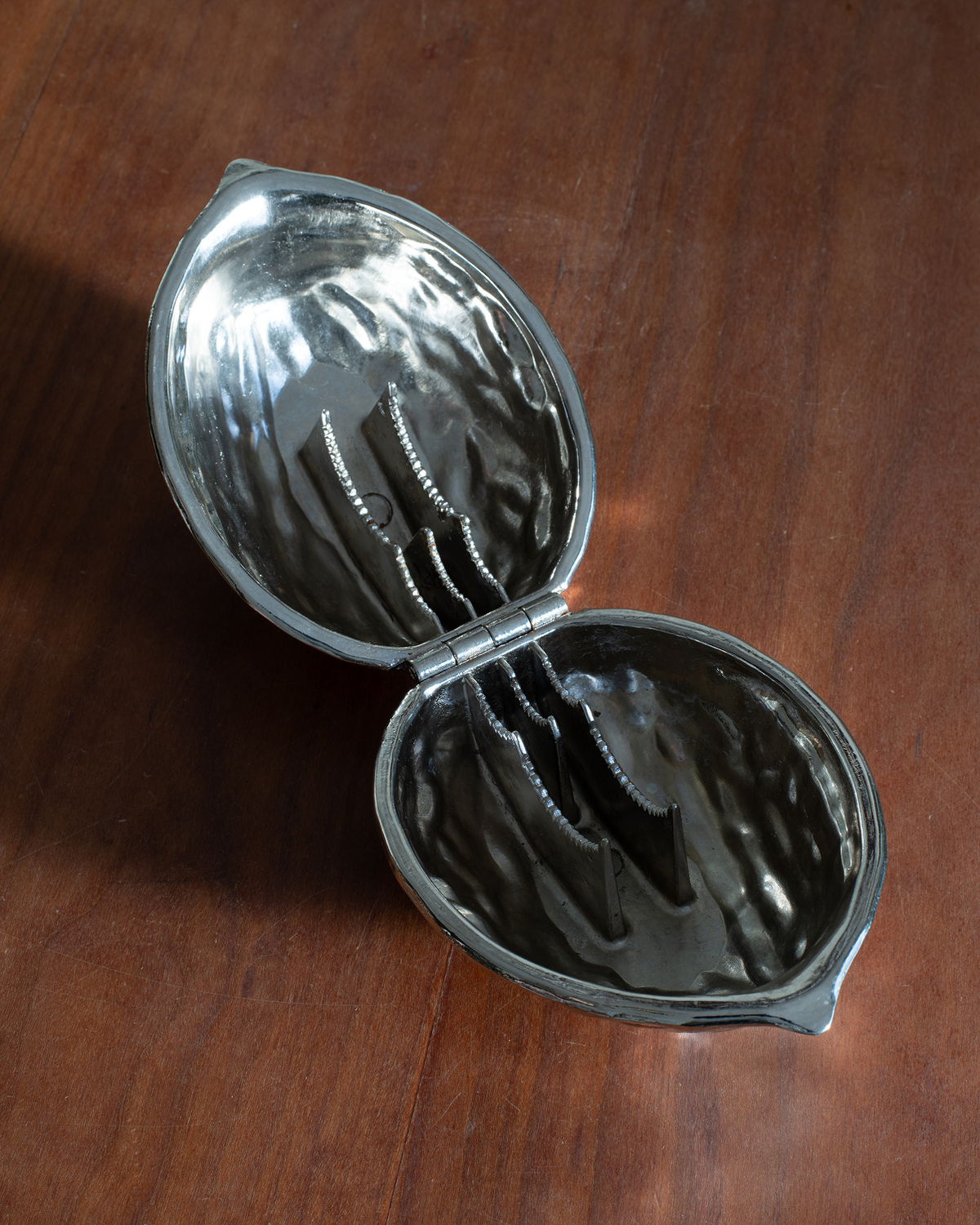 A silver metal walnut-shaped mold, shown open on a dark brown wooden surface.