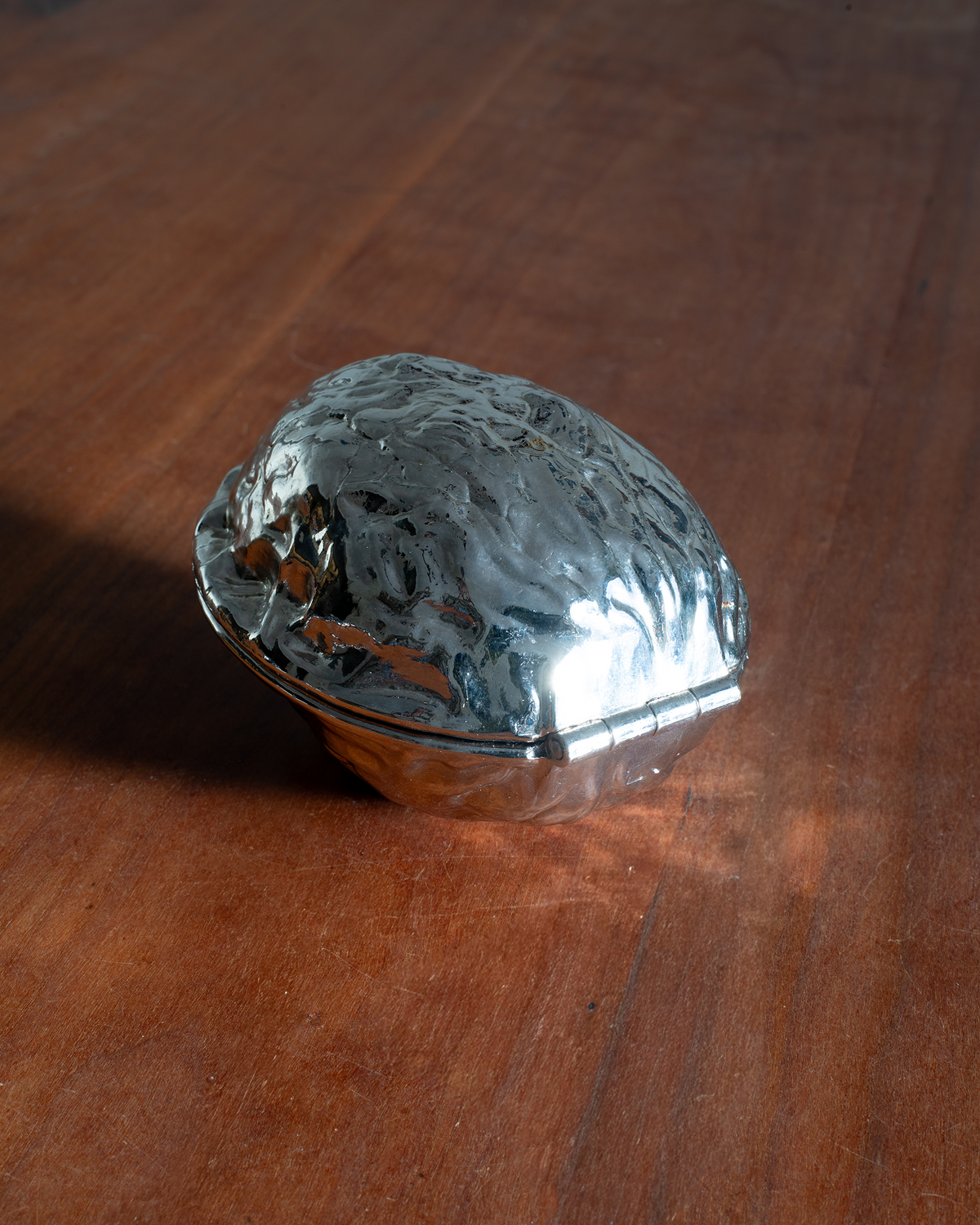 A small metallic silver box with a textured, hammered finish and a hinge closure, resting on a polished wooden surface.