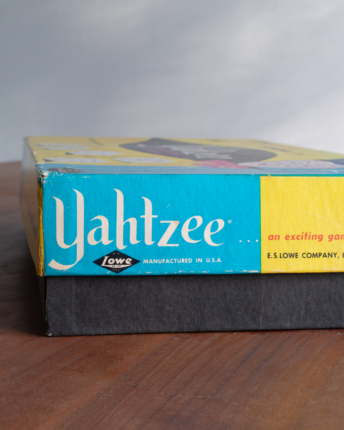 Vintage E.S. Lowe Company Yahtzee game box on a wooden tabletop with a blurred gray background.