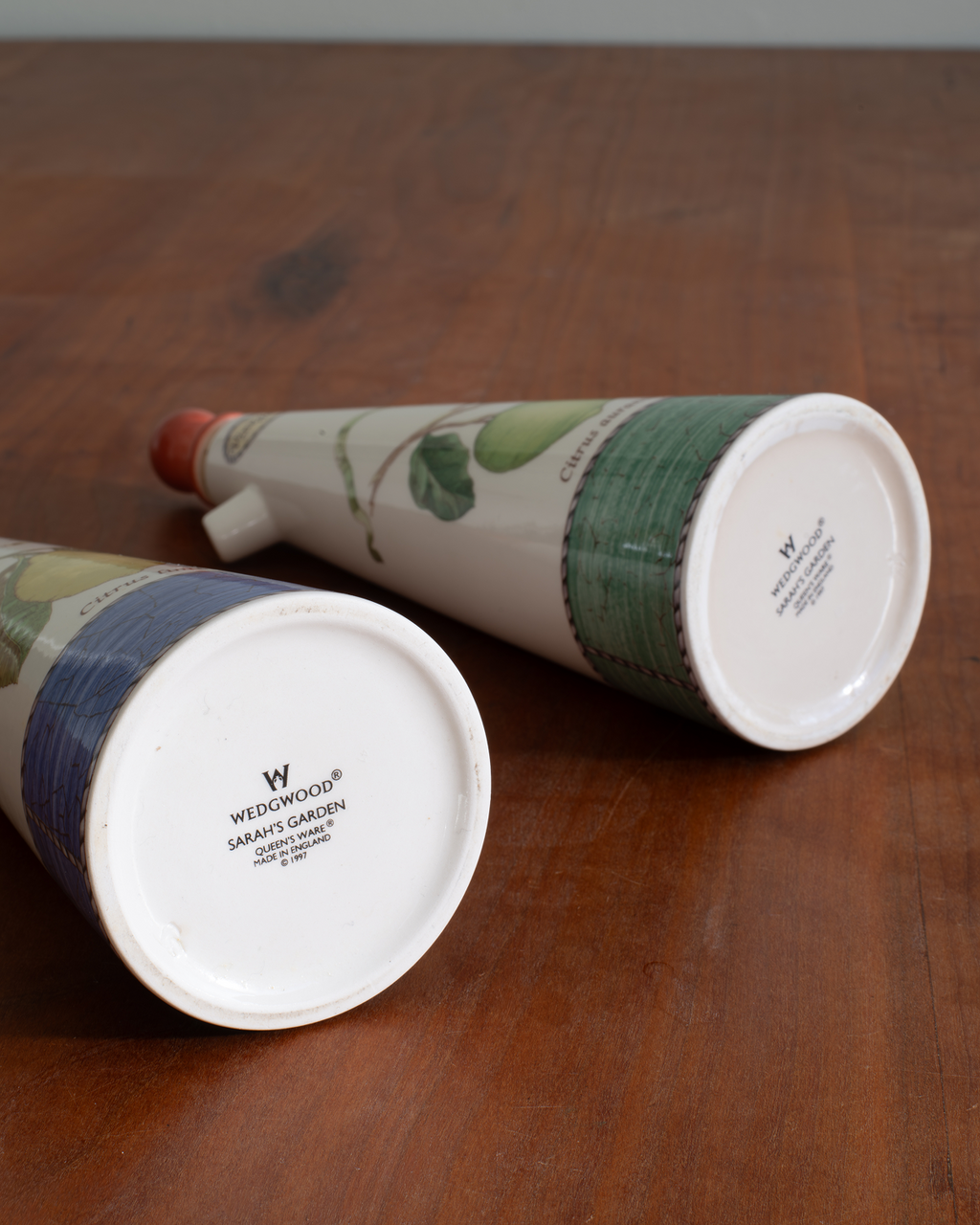 Two Wedwoodwood ceramic garden planters shaped like conical flower pots, displayed on a wooden tabletop. One planter is lying on its side showing the white base with the Wedwoodwood brand name, and the other is angled to show its green and blue patterned upper body.