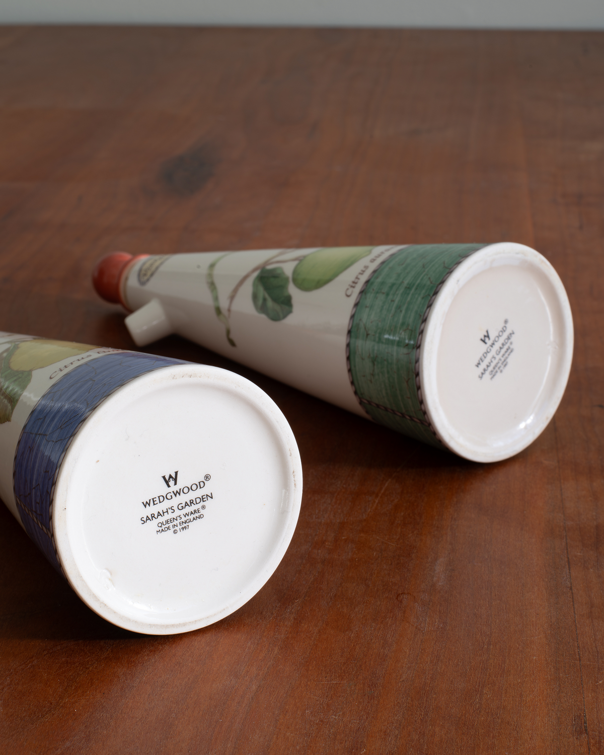 Two Wedwoodwood ceramic garden planters shaped like conical flower pots, displayed on a wooden tabletop. One planter is lying on its side showing the white base with the Wedwoodwood brand name, and the other is angled to show its green and blue patterned upper body.