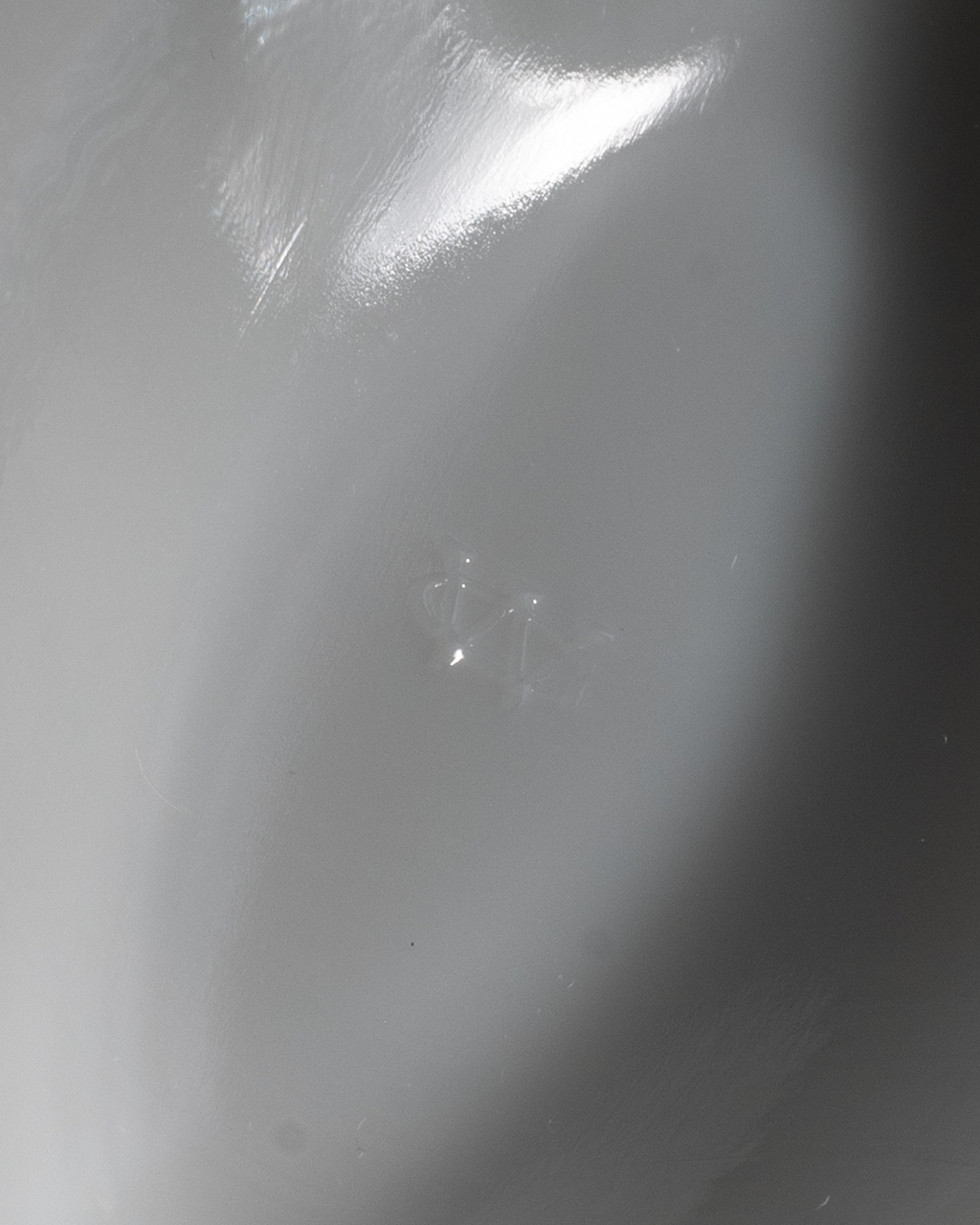 A close-up of a glossy, light gray surface with a bright reflection and a small, faint logo or mark in the center.