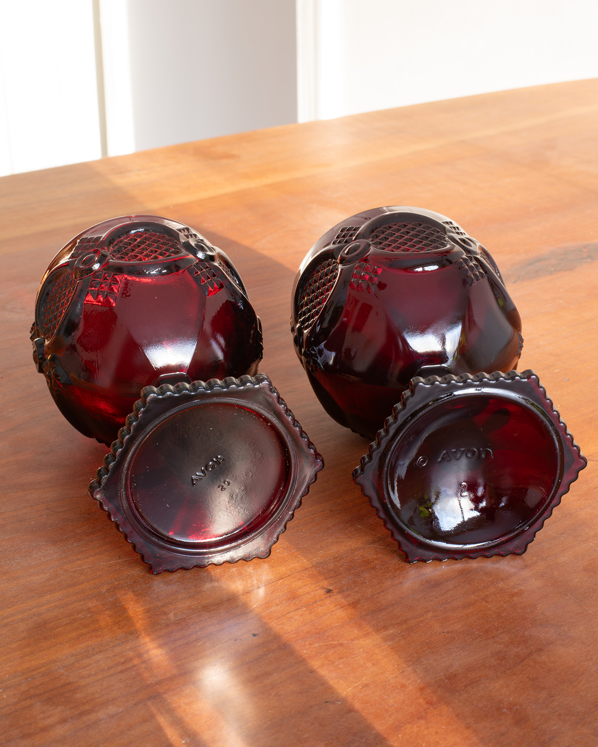 Three vintage dark red glass punch glasses with decorative cut patterns, arranged on a wooden table.