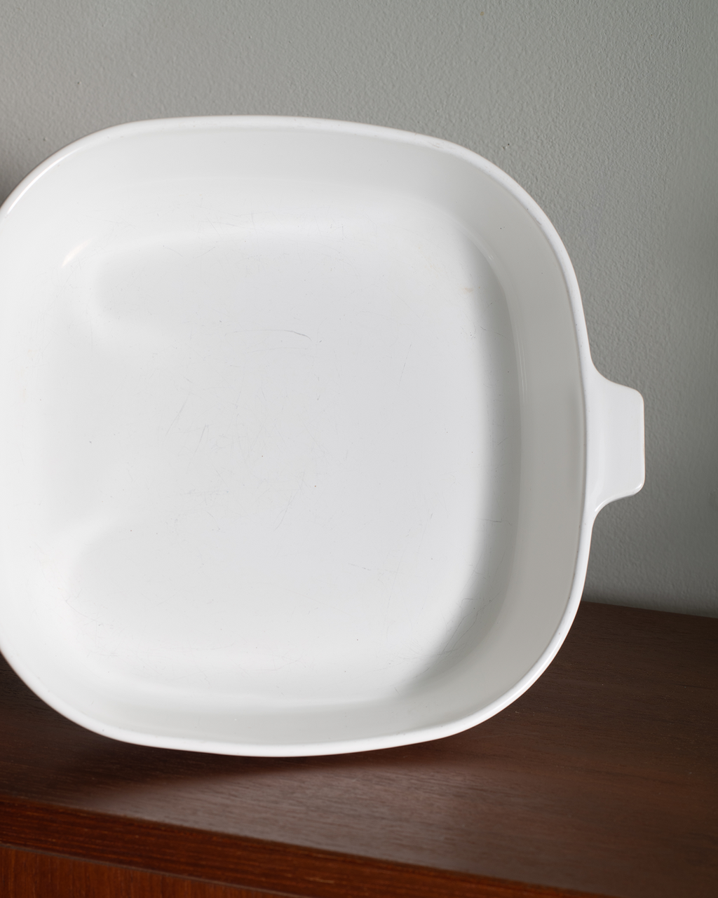 A white oval casserole dish decorated with a blue floral pattern, sitting on a wooden shelf against a light gray wall.