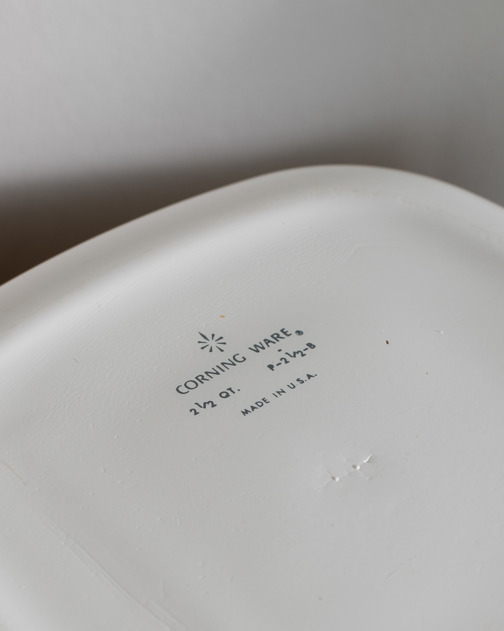 Close-up of the inside bottom of a white ceramic dish or plate, showing printed text that reads CORNING WARE with a small starburst logo, along with size and made-in-USA information.