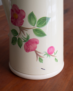 A close-up of a cream-colored thermos decorated with pink flowers and green leaves, resting on a wooden surface.