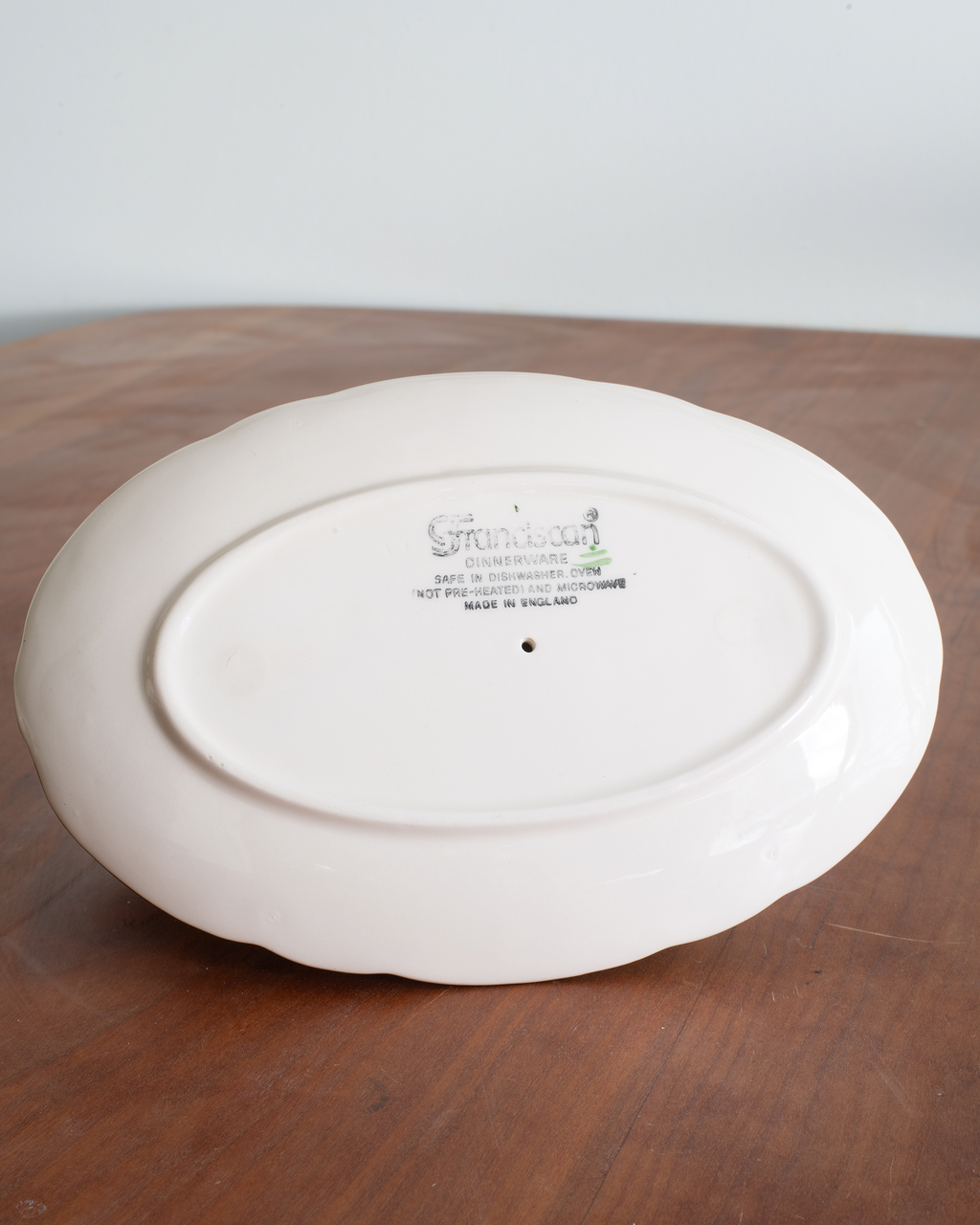 The underside of a white ceramic gravy boat with a scalloped rim, resting on a wooden surface. The brand name 'Franciscan' is printed in the center.