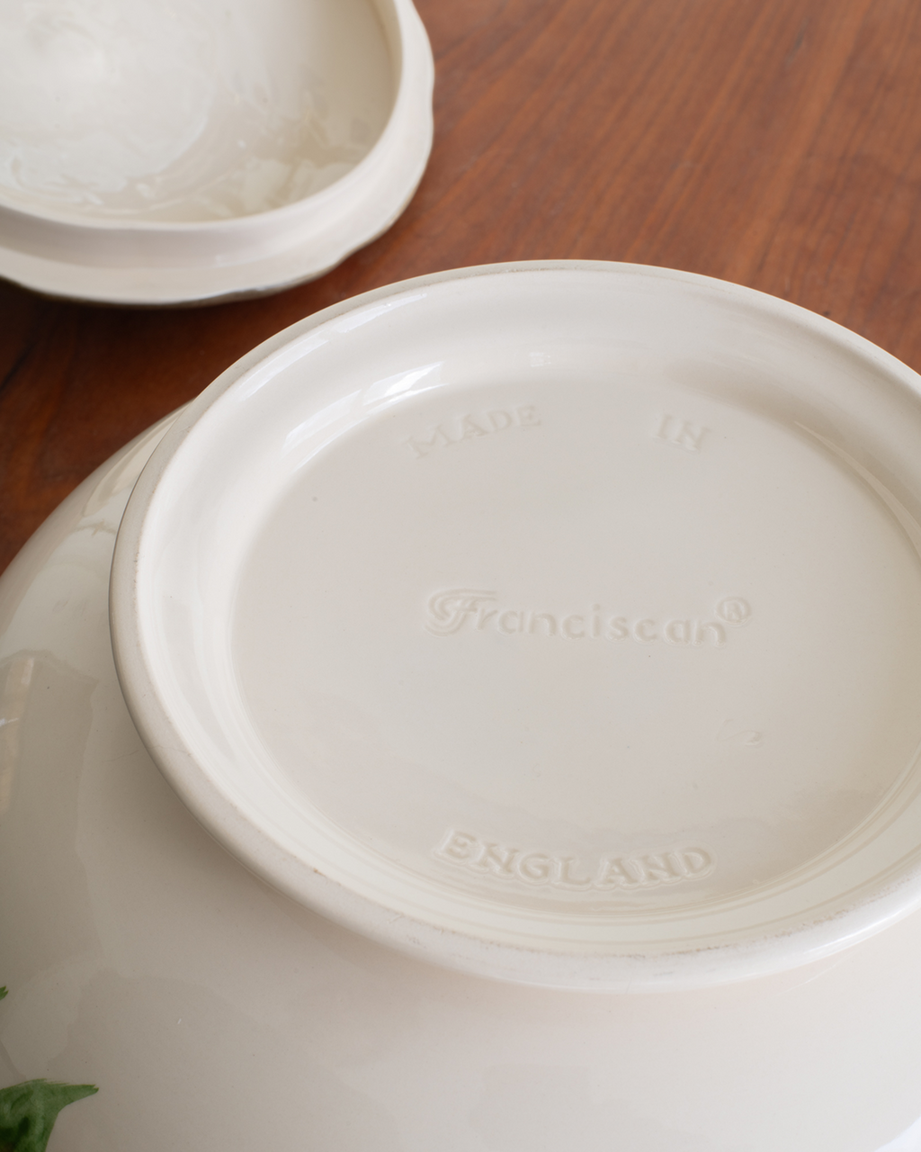 Close-up of the inside bottom of a white ceramic toureen, showing the embossed brand name 'Franciscan' and 'MADE IN ENGLAND' on a wooden table.
