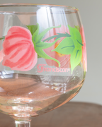 A close-up of a clear stemmed glass with a pink rose and green leaves hand-painted on the bowl, featuring the word 'Francesco' in pink script.