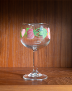 A clear stemmed wine glass with a colorful floral pattern of pink tulips and green leaves, featuring the brand name 'francocini' printed on the side, set against a warm wooden background.