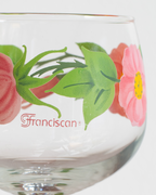 A close-up of a clear glass bowl or cup featuring a printed floral design with pink flowers, green leaves, and the word 'Franciscan' in red script near the bottom.